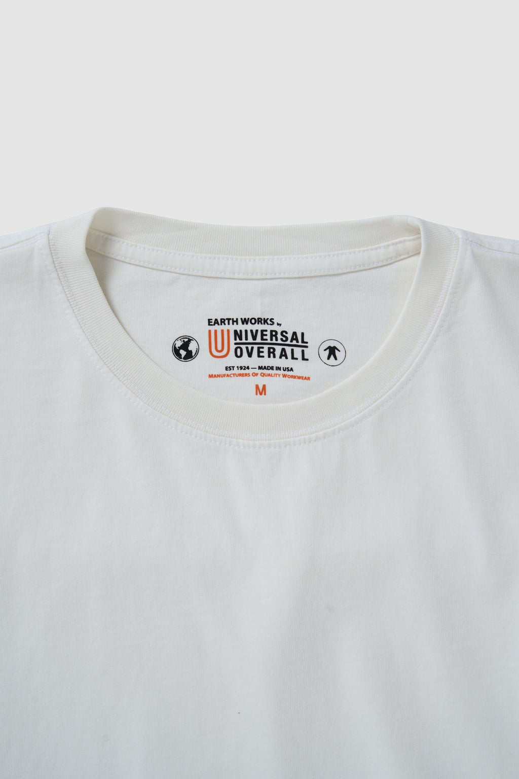 Close-up of a white t-shirt with a brand logo on the collar against a light gray background