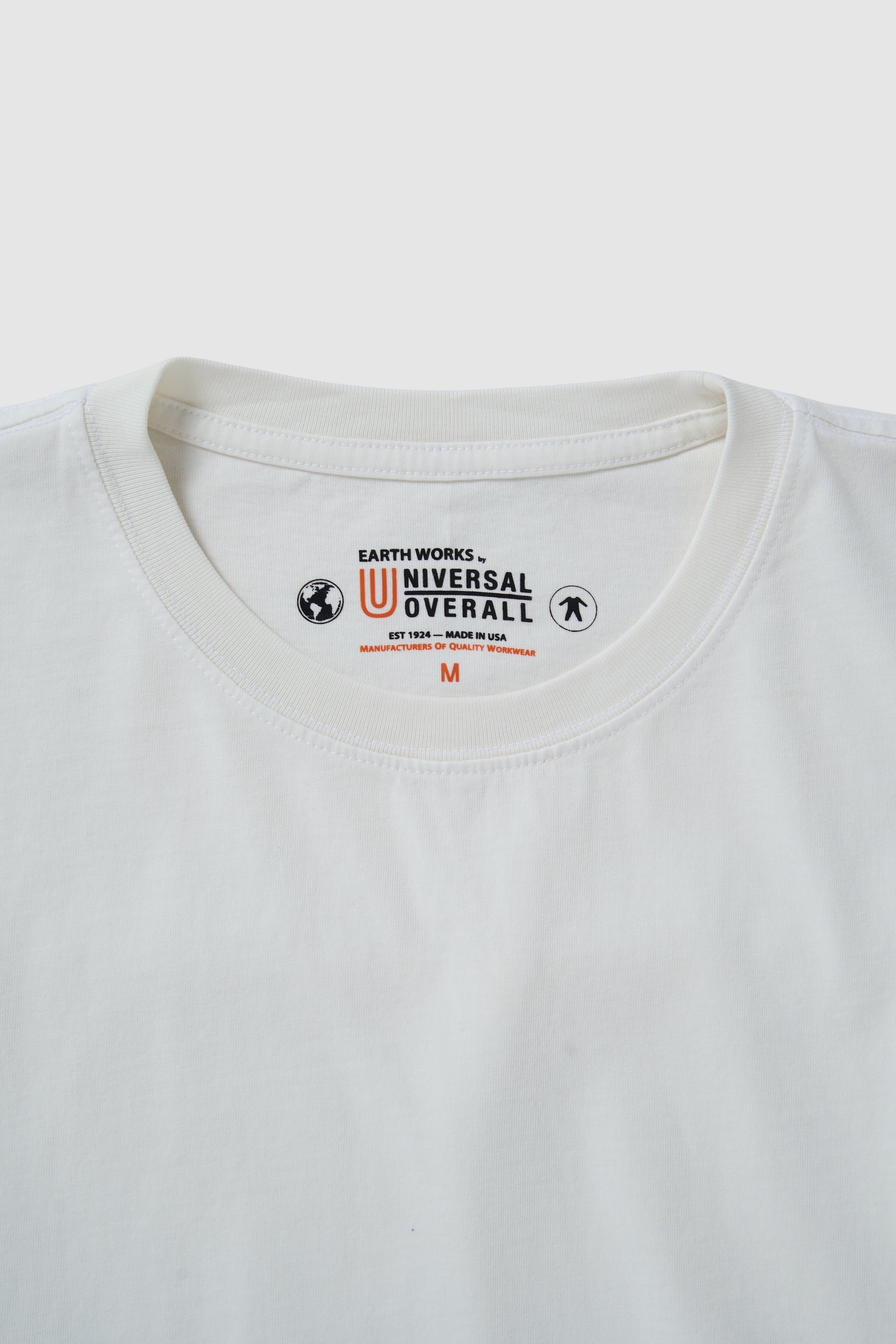 Close-up of a white t-shirt with a brand logo on the collar against a light gray background